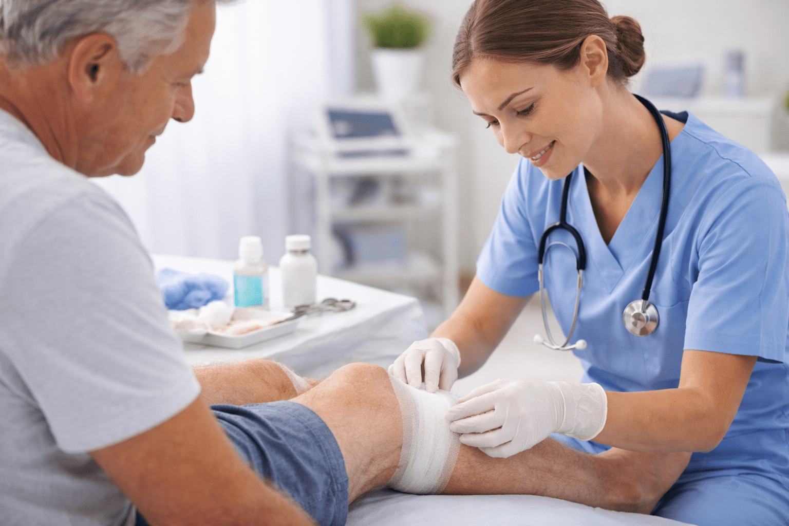 Compassionate mobile wound care specialist applying a clean bandage to a patient’s leg in a professional medical clinic.